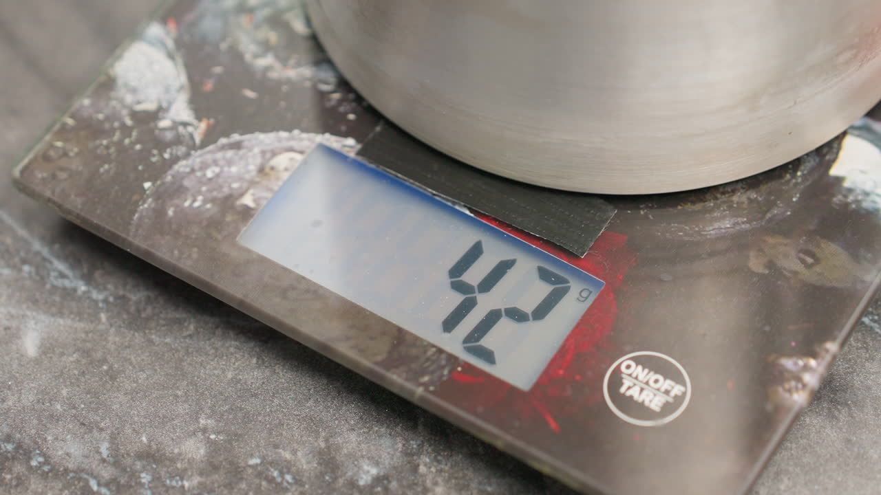 Close up of kitchen digital weighing scale displaying zero with metallic container placed on top, sitting on dark textured countertop, used for precise measurement in culinary or craft activities