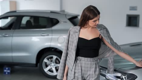 elegante mujer joven de moda posando cerca del coche en un concesionario de coches