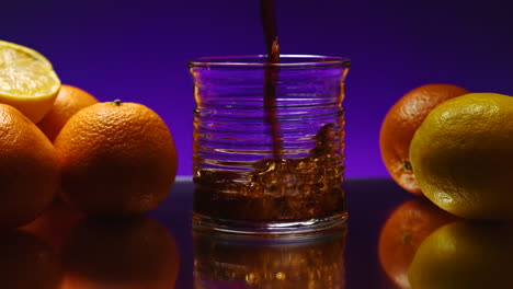 pouring soda into a glass surrounded by citrus fruits