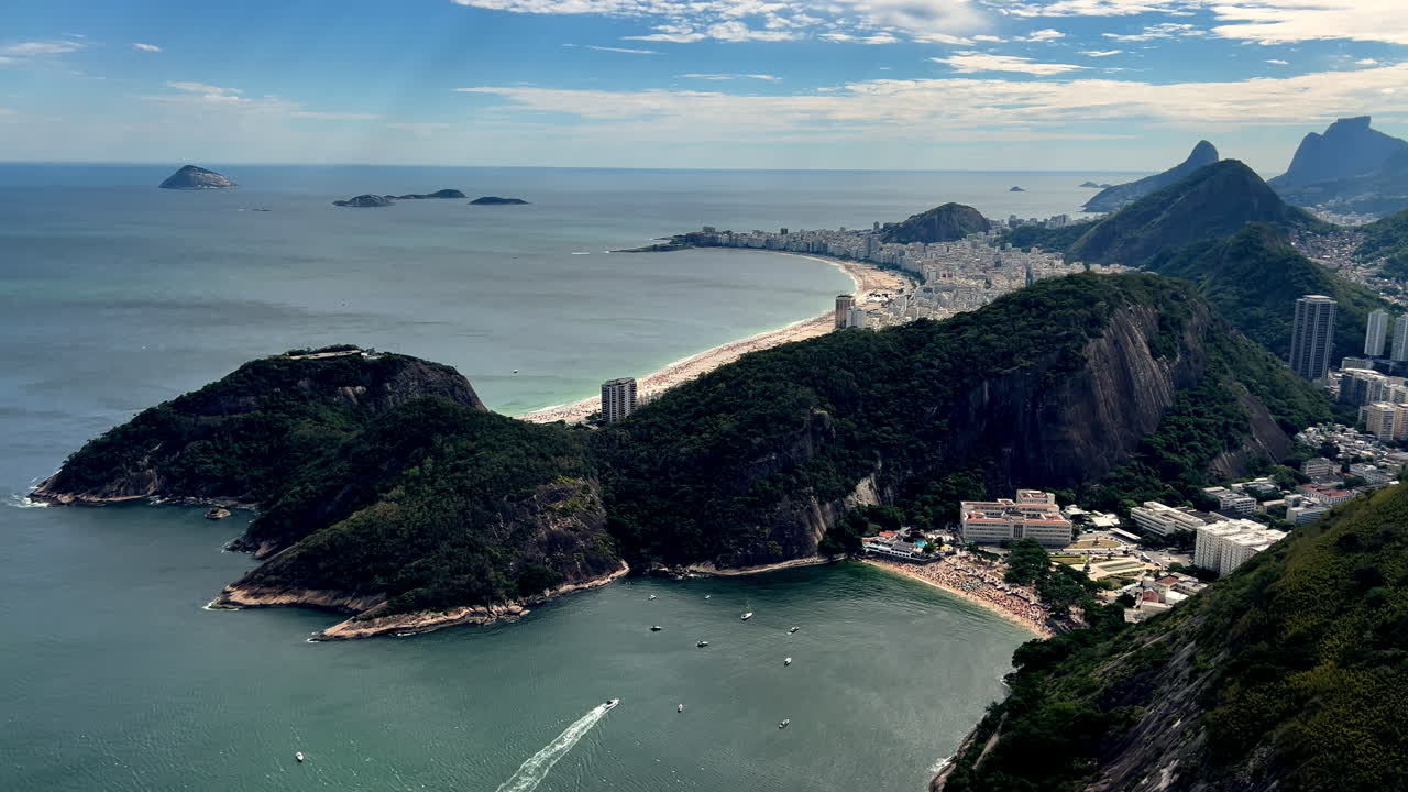 Inquadratura tilt-up a partire dalle acque smeraldine di Praia Vermelha che si alza per rivelare le iconiche spiagge a mezzaluna di Leme e Copacabana lungo la costa di Rio de Janeiro