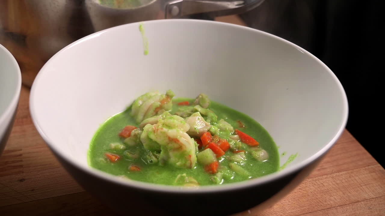 sirviendo más estofado de mariscos peruanos con caldo de cilantro en el tazón de sopa