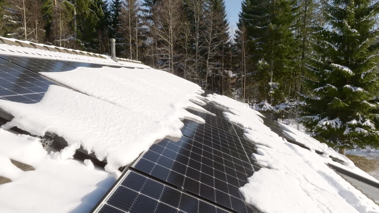 Aerial view over snowy solar cells on a house roof, melting in winter sunlight