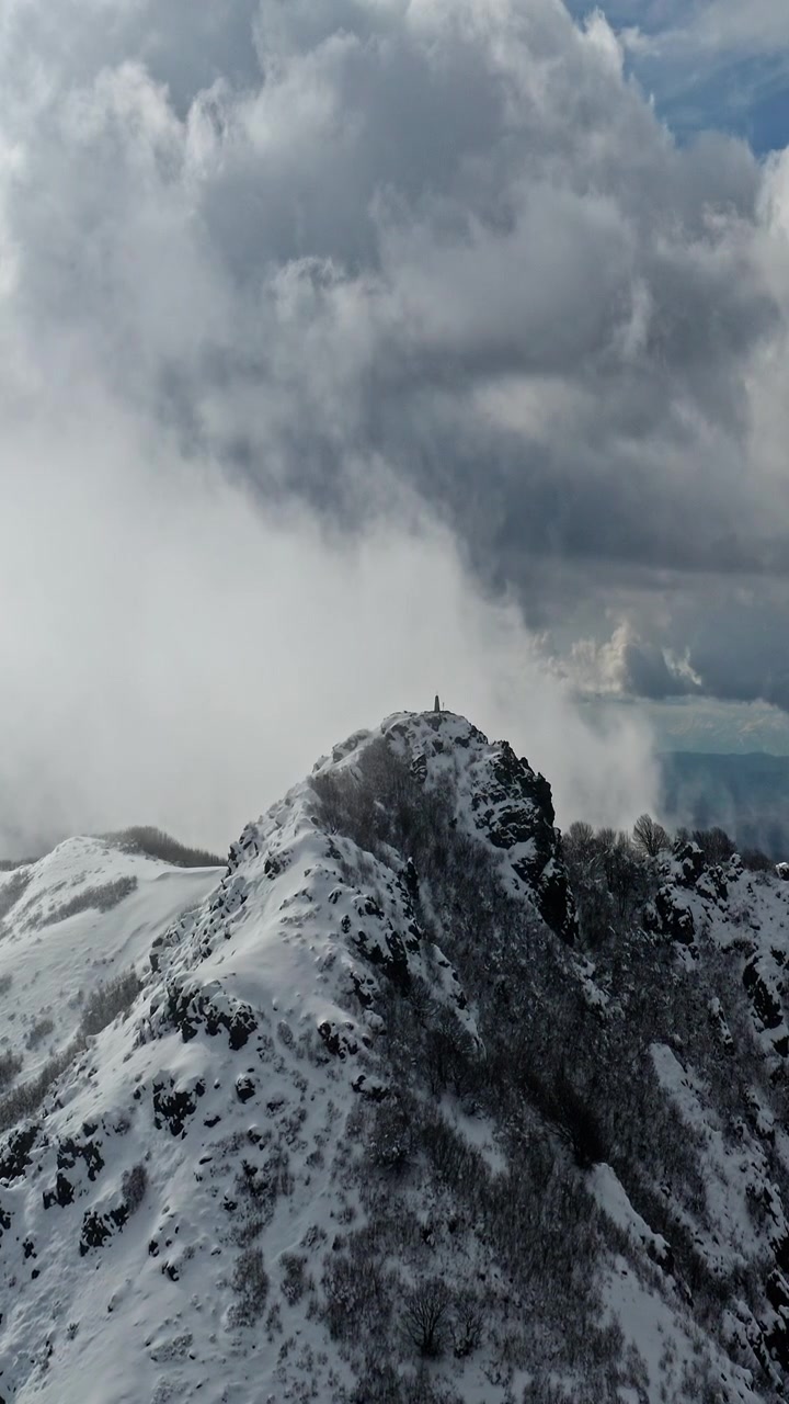 Una cima innevata si staglia contro nebbia e nuvole vorticose, creando una scena drammatica. Ideale per l'uso in film d'avventura o documentari che esplorano paesaggi remoti.