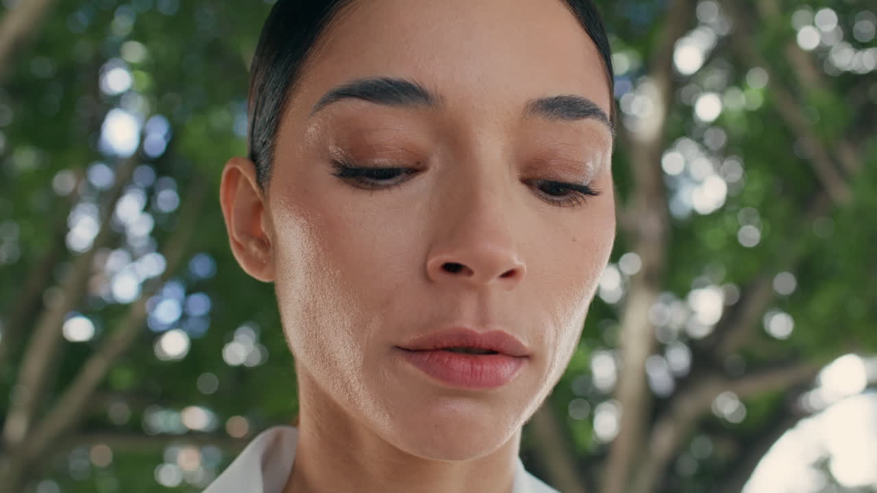 녹색 나무 앞에 서 있는 매력적인 슬픈 여자. 아래로 보는 소녀