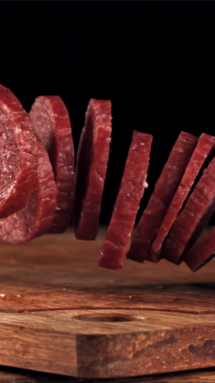 Fette di salame che cadono su un tagliere di legno al rallentatore