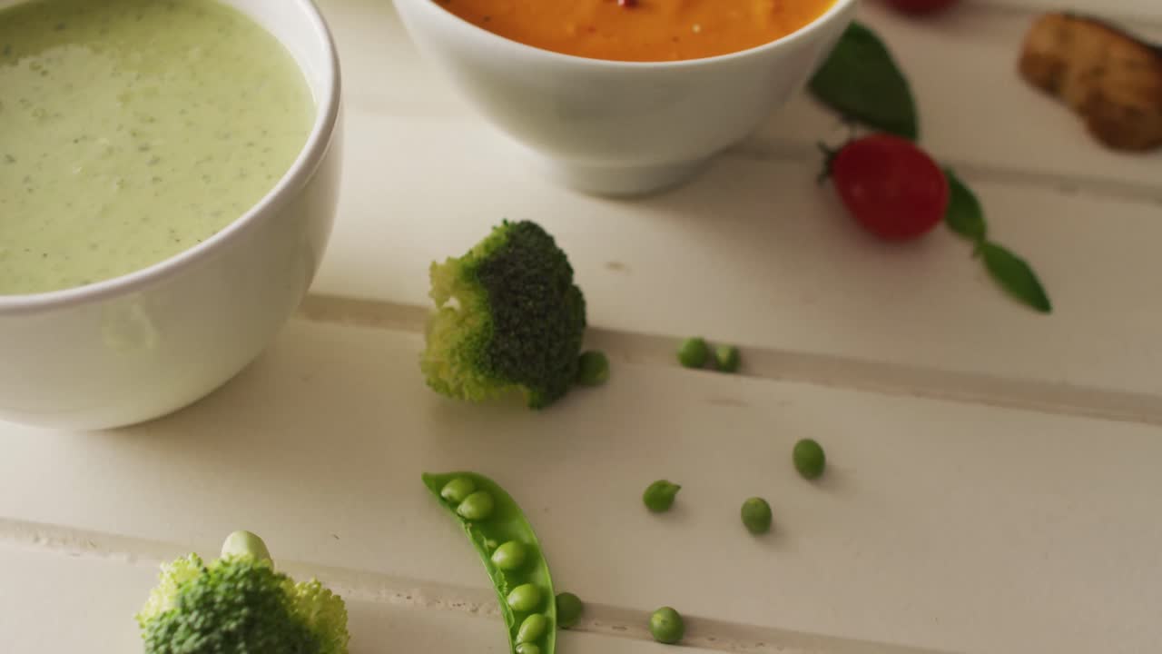 Video of diverse cream vegetable soups with ingredients lying on white surface