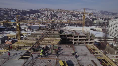 Überfliegen-Der-Baustelle-Mit-Arbeitern-Und-Kran,-Der-Im-Winter-Baumaterialien-Transportiert