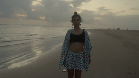 an indian woman gracefully walks along the beach, nearing the camera with the sea as her tranquil backdrop