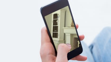 persona que sostiene un teléfono inteligente con interiores modernos de la sala de estar mostrados en la pantalla