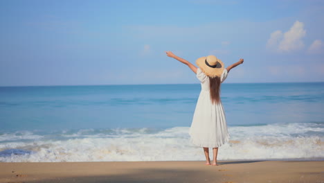 Woman-on-seashore-raising-arms-and-looking-at-horizon-while-waves-crash