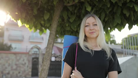 portrait of a beautiful blonde holding a fitness mat and looking at the camera a sports girl portrait of a beautiful blonde holding a fitness mat and looking at the camera a sports girl on a morning workout fitness concept