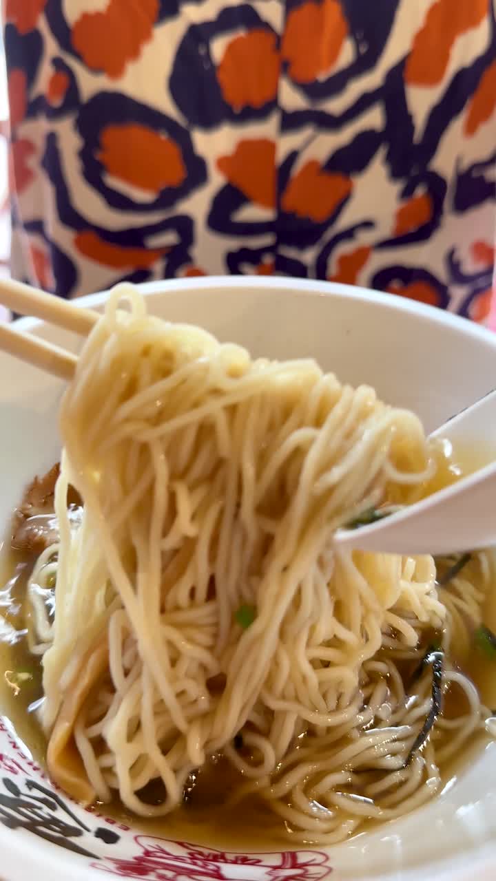箸で丼からラーメンの麺を持ち上げる手、鮮やかな背景、浅い被写界深度。
