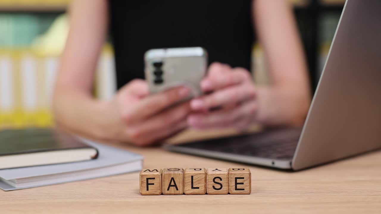 Woman using mobile phone with the word 'FALSE' in wooden blocks on the desk