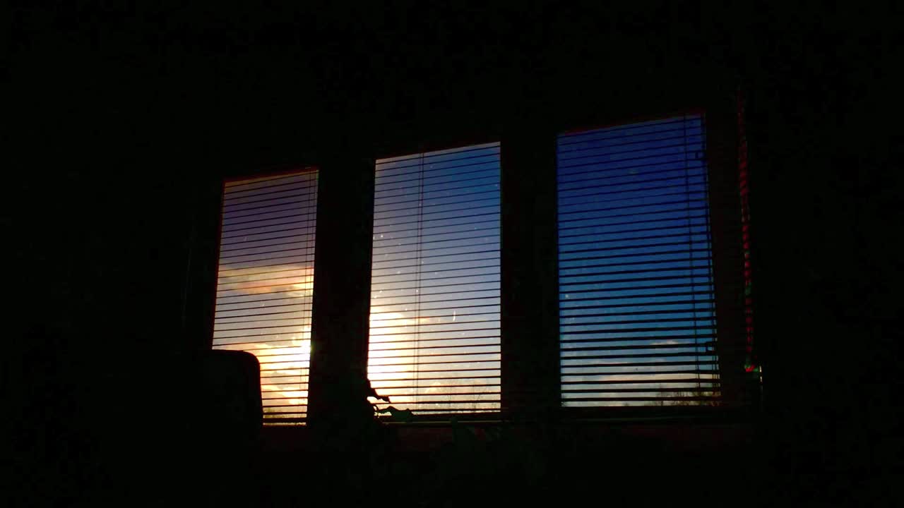 Early morning time lapse of sun moving, shot through open blinds in a dark room, looking at sky and clouds, with lens flare at end