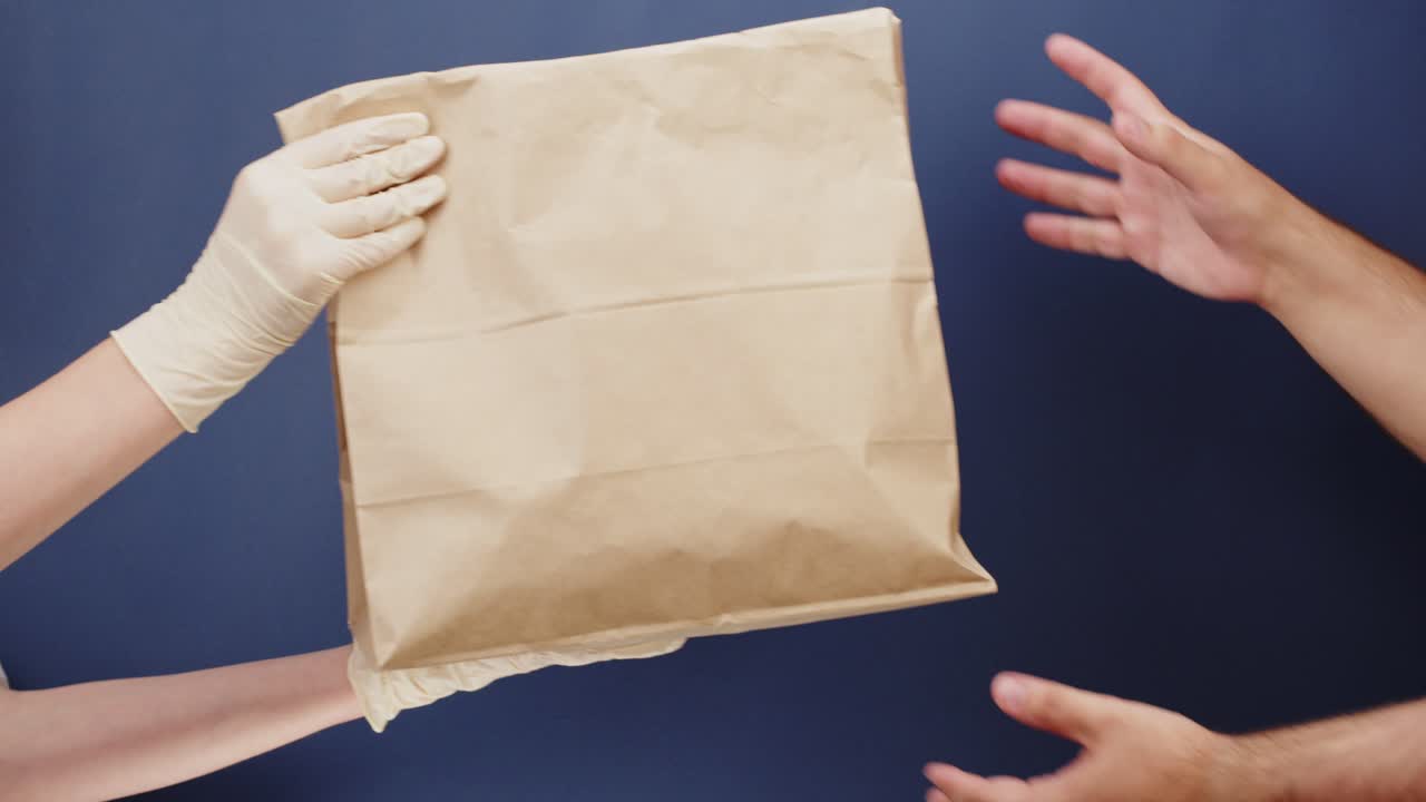 Gloved Hands Delivering Brown Paper Bag to Another Person
