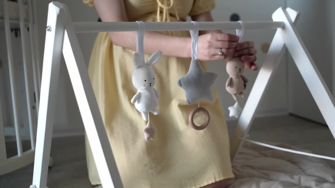 mujer embarazada colgando juguetes de peluche en el gimnasio de juego de bebé hecho de madera en el vivero