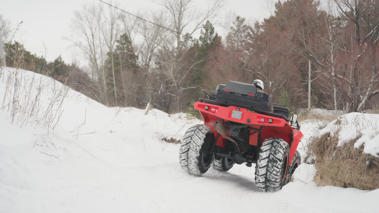 Un ATV rosso si arrampica su una sponda innevata, le ruote anteriori scavano e le sospensioni si flettono, la coppia del motore si sforza di salire. Un'inquadratura ravvicinata mostra il battistrada e il movimento dell'asse, mentre il pilota gestisce l'acceleratore e l'equilibrio durante un fuoristrada estremo.