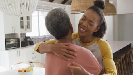 african american mother and daughter hugging each other in the kitchen at home