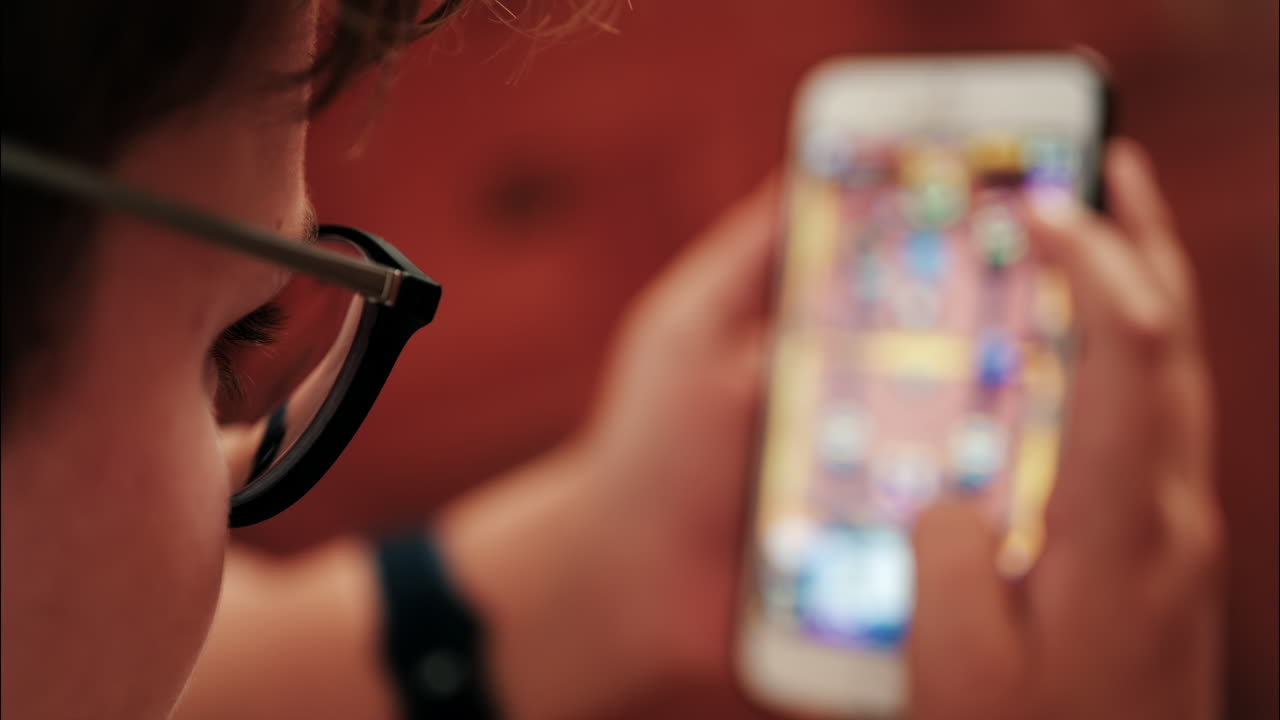 Over-the-shoulder close-up of a kid with glasses playing on a smartphone indoors