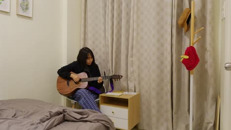 beautiful asian guitarist practicing with acoustic guitar in corner of room