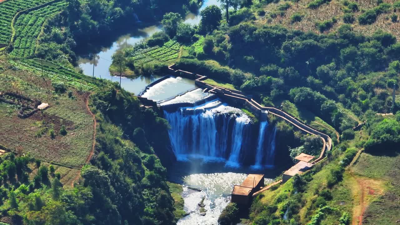 Drone shot of a cascading waterfall surrounded by vibrant farmland and lush green vegetation in Madagascar. Scenic rural landscape ideal for eco-travel, agriculture, or nature projects.