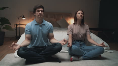 young couple meditating, woman and man sharing moments in lotus pose indoors