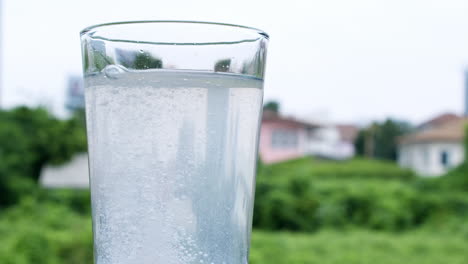 agua burbujeante en un vaso causada por la dilución de un antiácido o bicarbonato de sodio en un telón de fondo de casas y vegetación verde fuera de foco