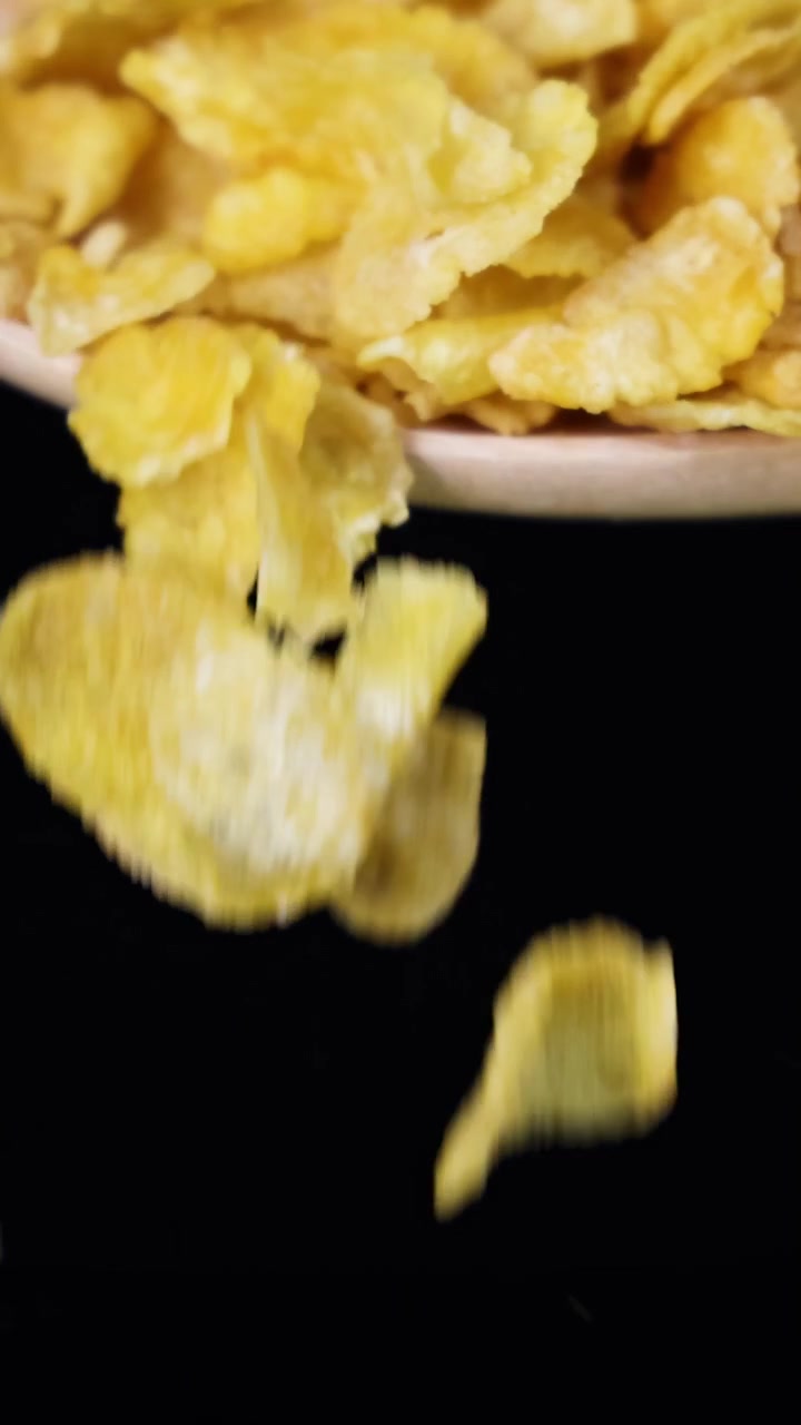 Corn cereal flakes tumble from a spoon against a black background, captured in slow motion with dramatic lighting