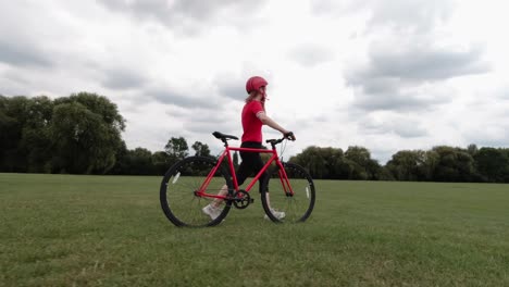 Caucasian-female-cyclist-in-red-top-walking-with-her-bike-in-a-park