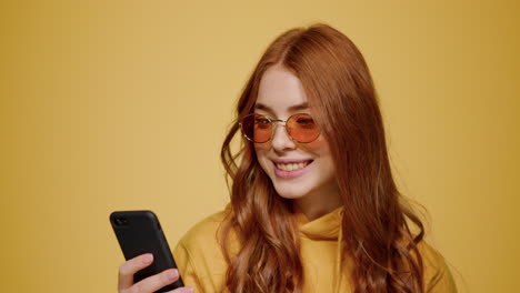 Redhead-girl-holding-smartphone-in-studio.-Woman-reading-message-on-mobile-phone