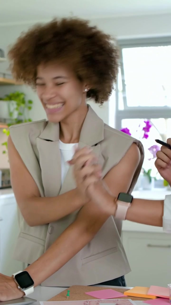 Vídeo vertical: Mulher de colete digitando na cozinha enquanto colega aponta para o laptop, com anotações para o projeto.