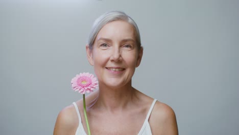 una mujer mayor sonriente con una flor rosa.