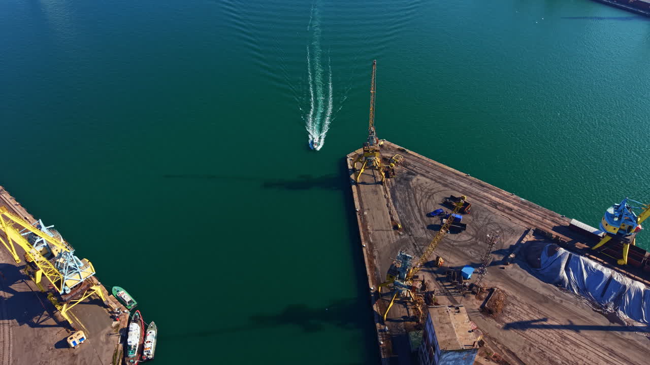 View of a boat moving in the water with cranes and loading area at a port during the day