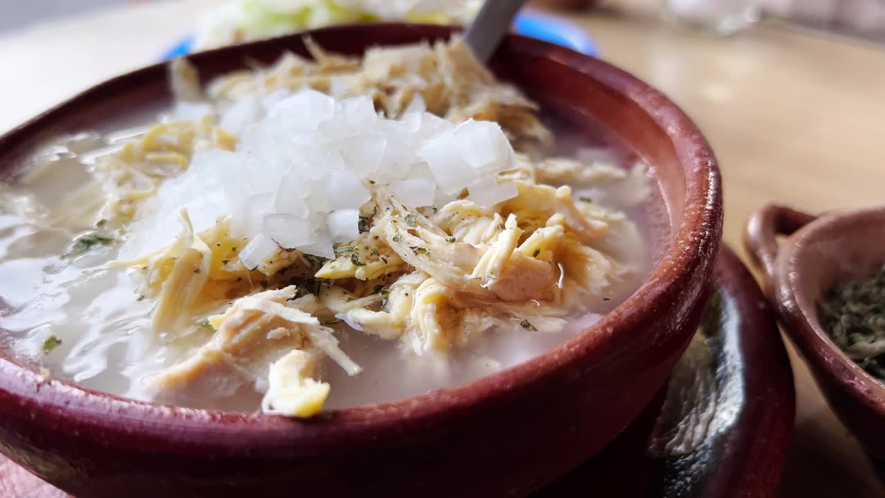 Bowl of white pozole being topped with onions, a classic Mexican dish