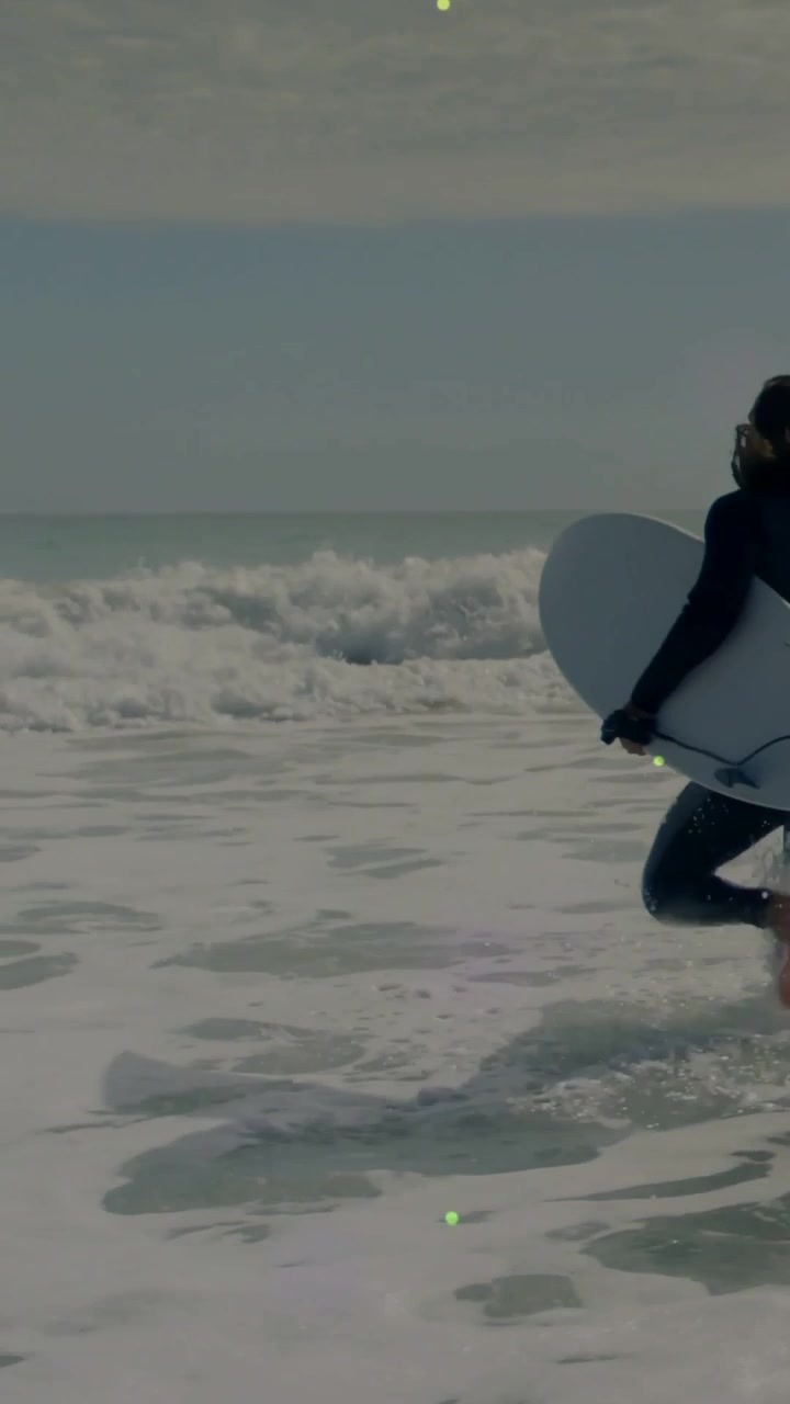 Video verticale: Surfista donna che cammina verso l'onda per fare surf, con bagliori della tavola che si muovono sulle gambe.