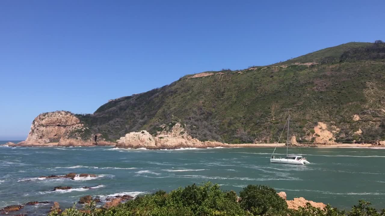 Veleiro catamarã se aproxima da barra do rio Knysna em maré forte e crescente.