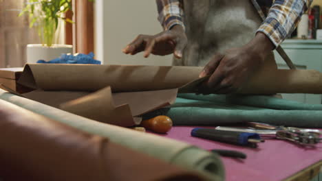 hands of african american craftsman in apron unrolling leather in leather workshop