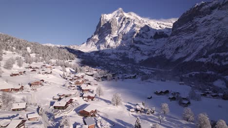 empujando sobre el nevado pueblo de montaña de grindelwald en un soleado día de invierno, volando hacia el monte wetterhorn en suiza