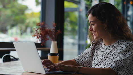 joven mujer de negocios sentada con una computadora portátil en una cafetería tomando una llamada en un teléfono móvil usando un micrófono