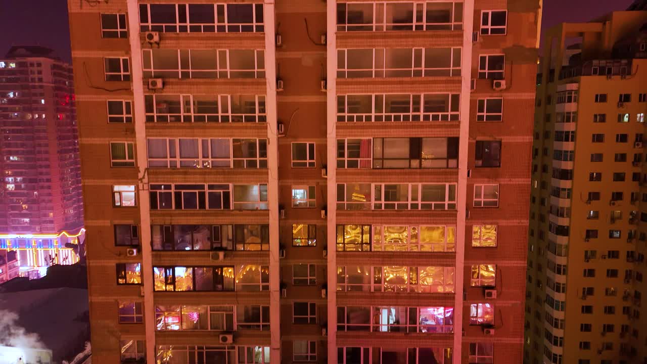 Drone view of an old high-rise apartment building in Harbin, China, with illuminated windows creating a warm, grid-like pattern.