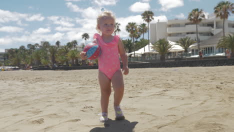 cute baby girl in pink swimsuit walking on the beach