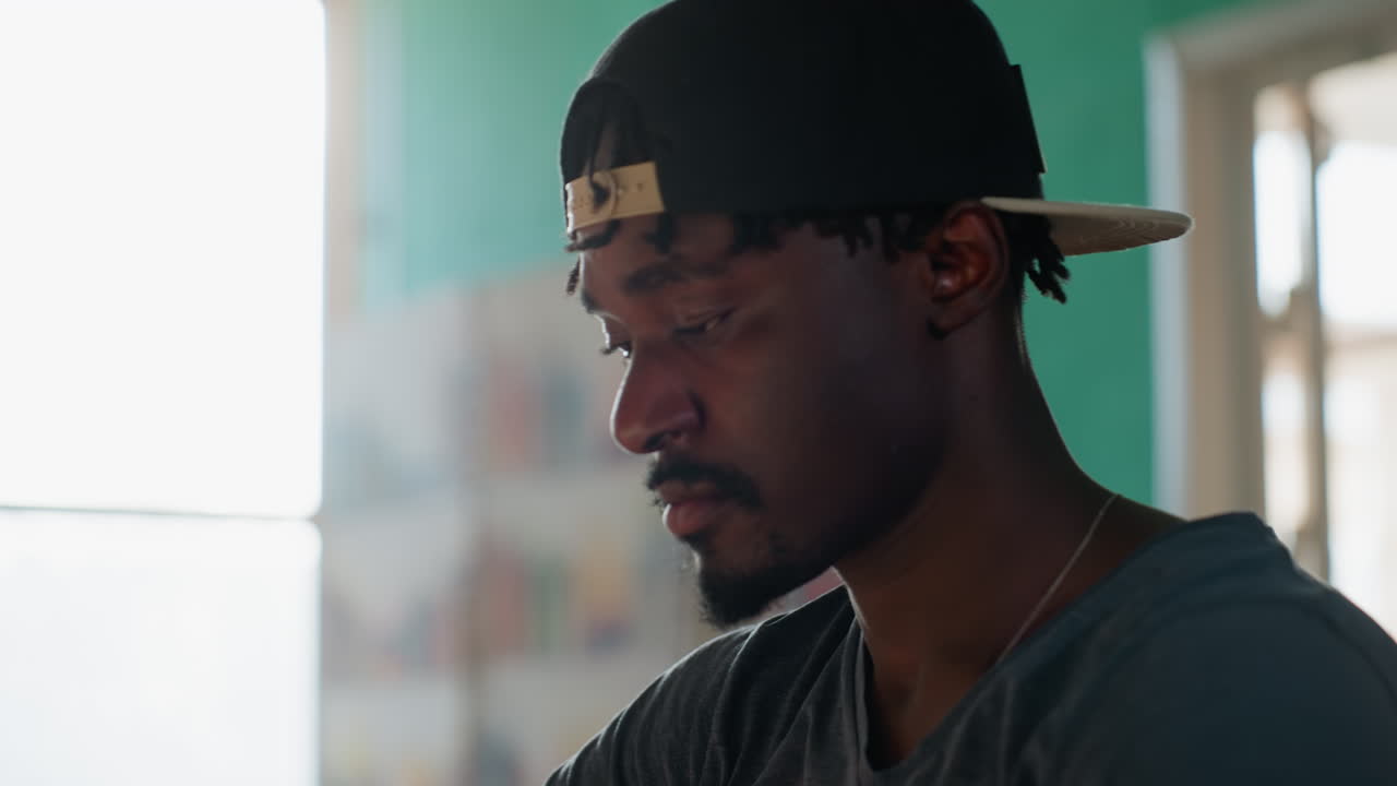 Close up of man in library stretching arms with eyes closed before resuming writing, seated at desk beside open book, taking short break from intense study in warm sunlight