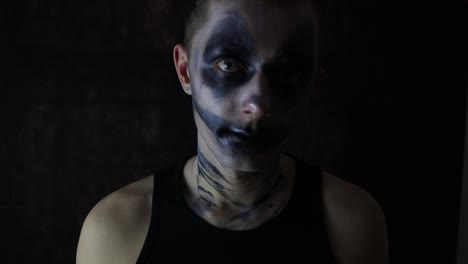 young man with a scary halloween dark clown makeup standing in front of a black background