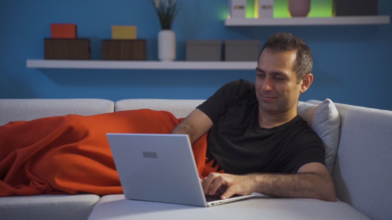 hombre feliz usando una computadora portátil acostado.