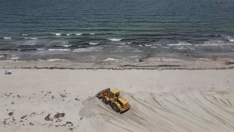 wheel loader pushing and reshaping sandy beach by pacific ocean in cohasset, massachusetts, usa