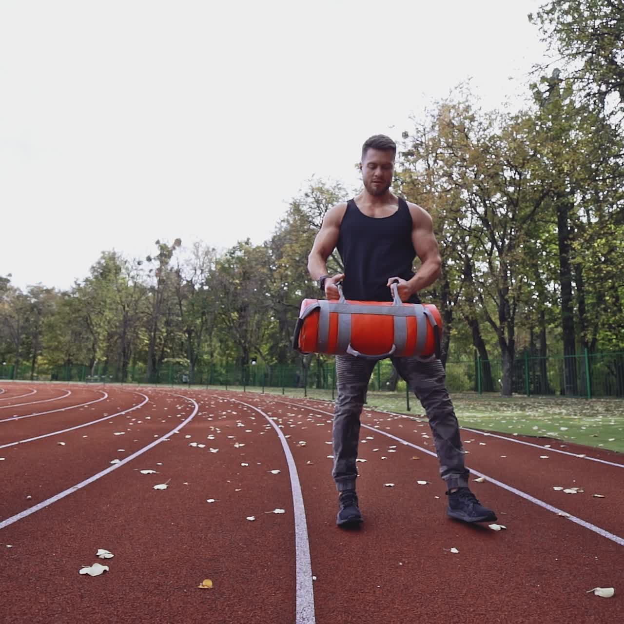 Athlete is doing workout in open air. Muscular sportsman lifting weights on the stadium in autumn daytime. Slow motion.