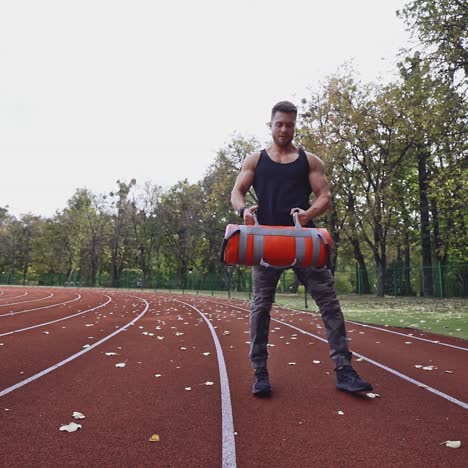 athlete is doing workout in open air. muscular sportsman lifting weights on the stadium in autumn daytime. slow motion.