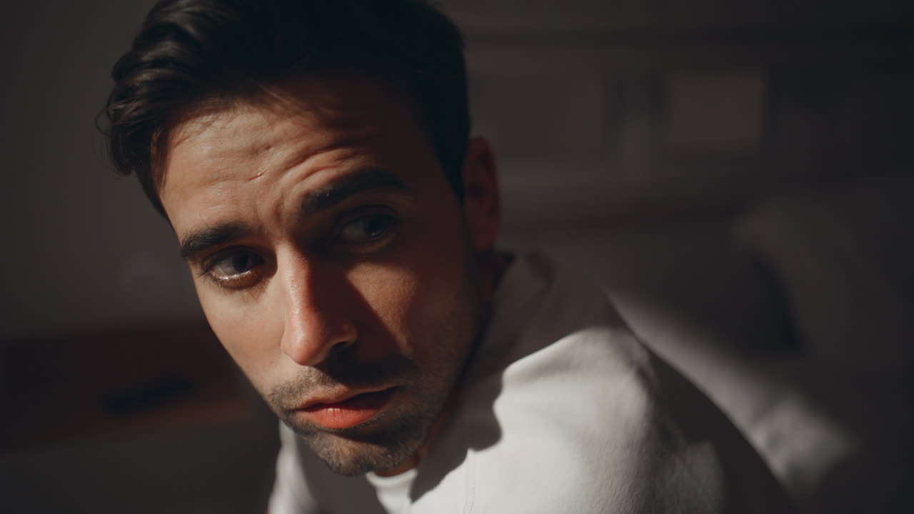 Pensive guy sitting bedroom looking window at moonlight closeup. Thoughtful man