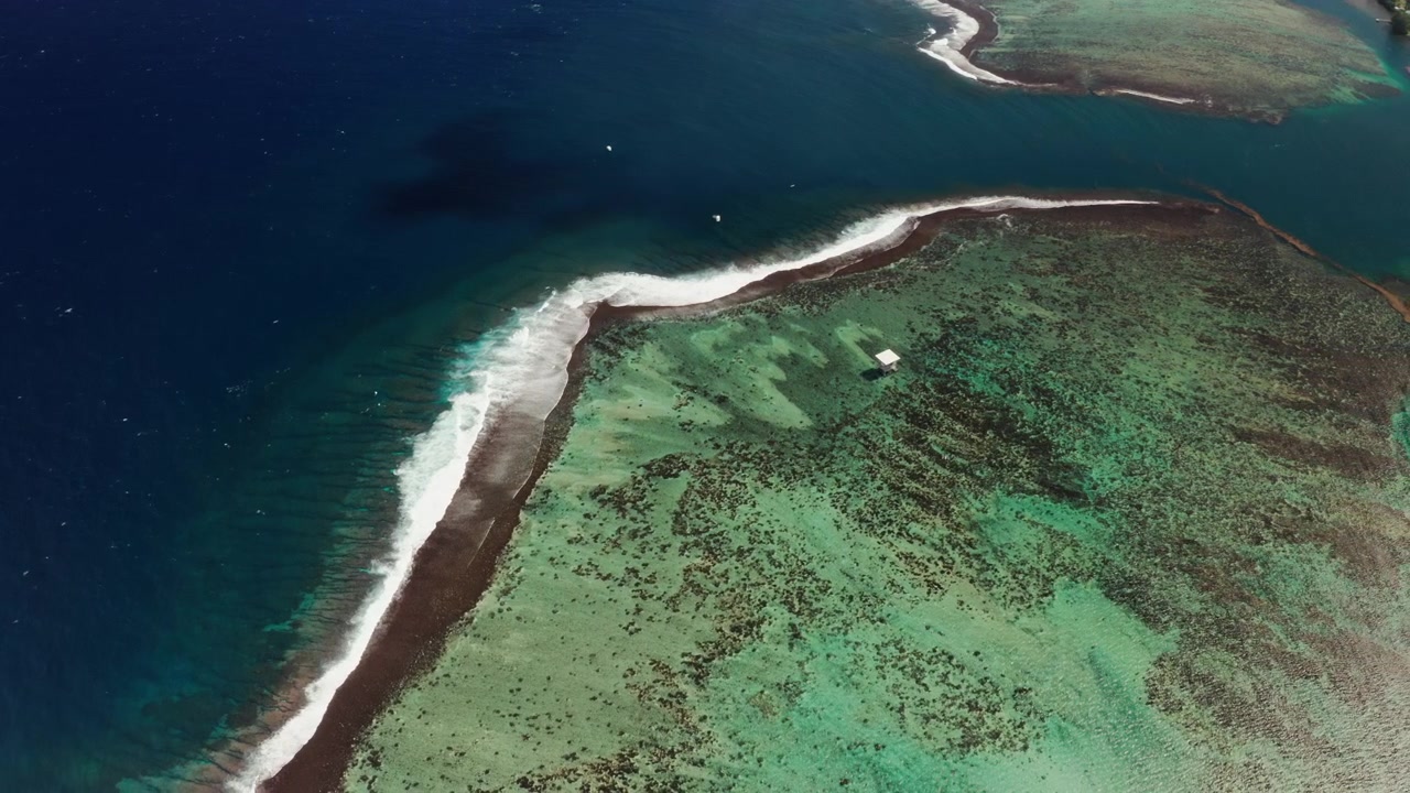 Tomada de drone em alta altitude sobre a passagem do recife de coral de Teahupoo, Tahiti, uma fina borda de recife branca separando as águas rasas da lagoa pálida do azul profundo do Pacífico