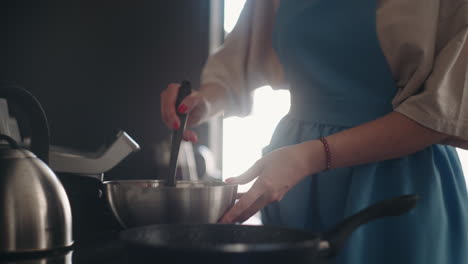 careful wife and mother is frying pancakes for breakfast in morning woman is pouring dough in pan